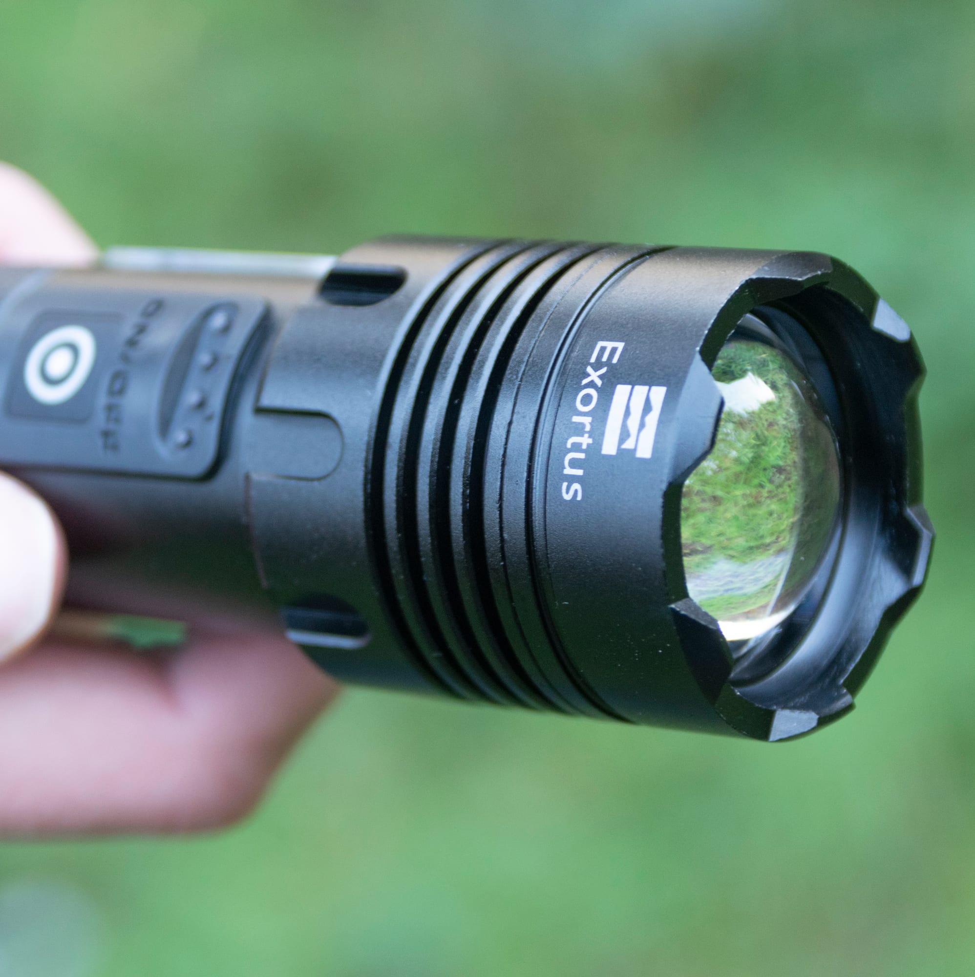 Exortus zaklamp met zoomkop van dichtbij vastgehouden in de hand, buiten in het groen